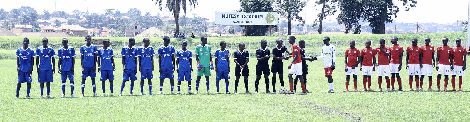 Both squads and the match officials stand across the pitch before kickoff at Mutesa II Stadium, Wankulukuku