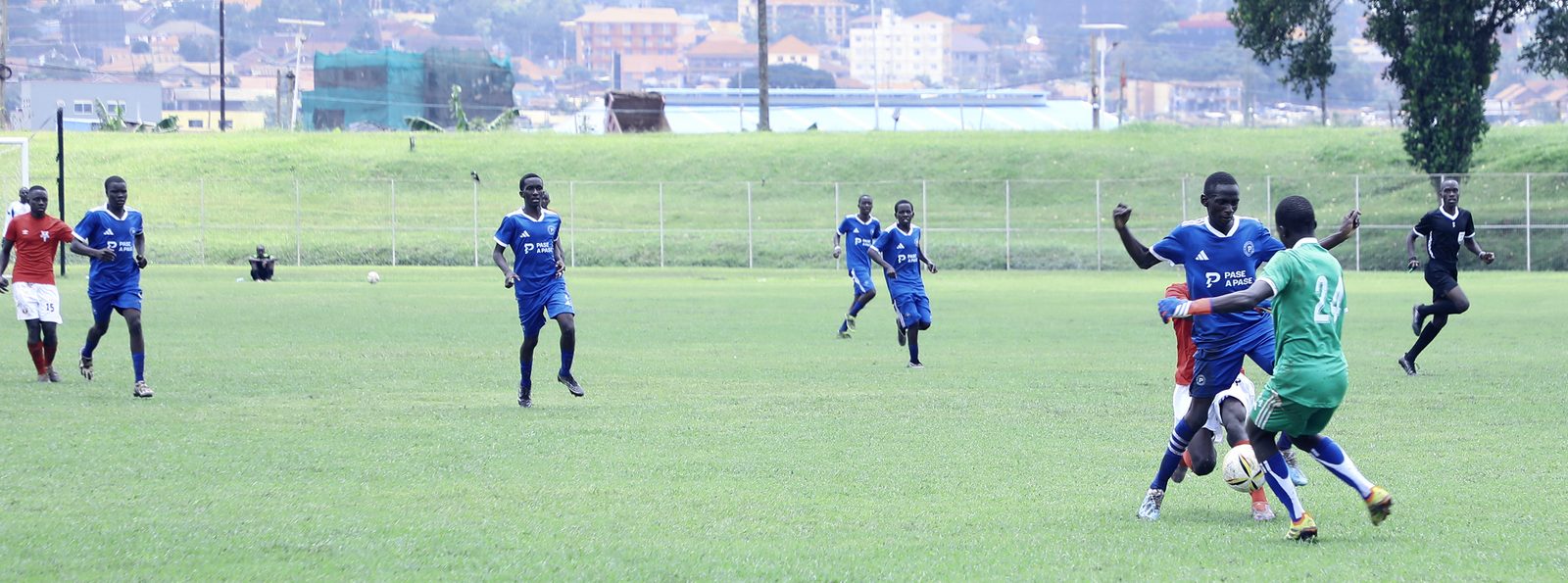 A PASE A PASE player shields the ball during a match, the Kampala hillside behind an open pitch